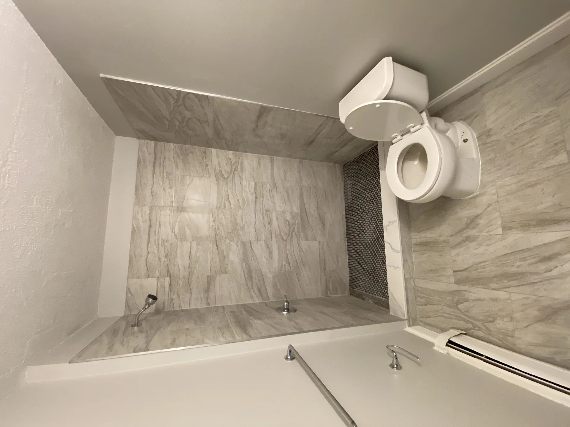 A newly remodeled bathroom featuring a walk-in shower with gray marble-look tiles and a white toilet. by SF Construction in S