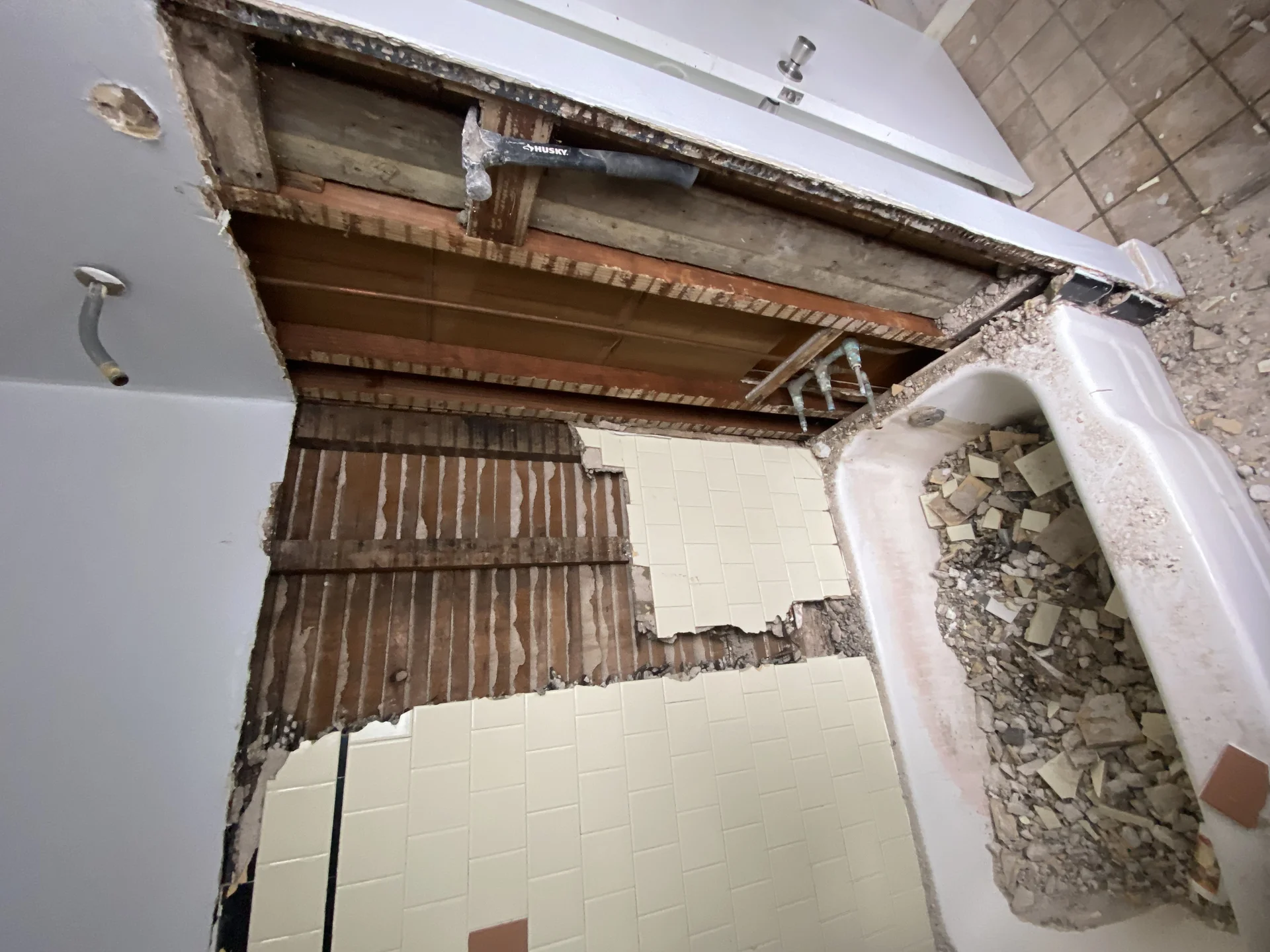 Bathroom during demolition with exposed lath and plaster, old tiles, and a bathtub full of debris. by SF Construction in Sudb
