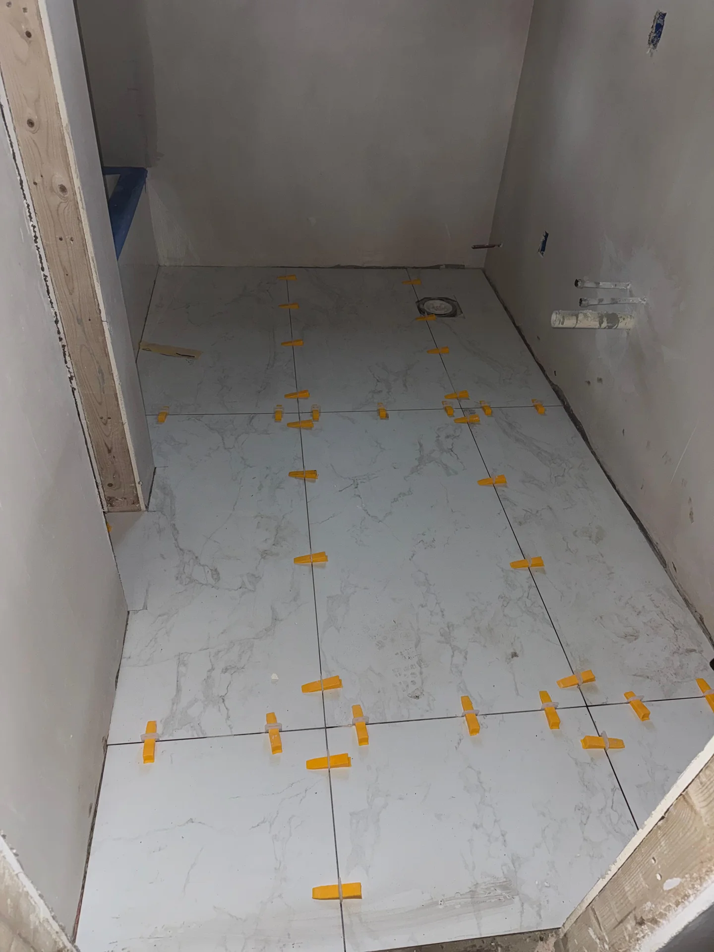Marble-look ceramic tiles being installed with yellow spacers and grout lines by SF Construction in Marlborough, MA