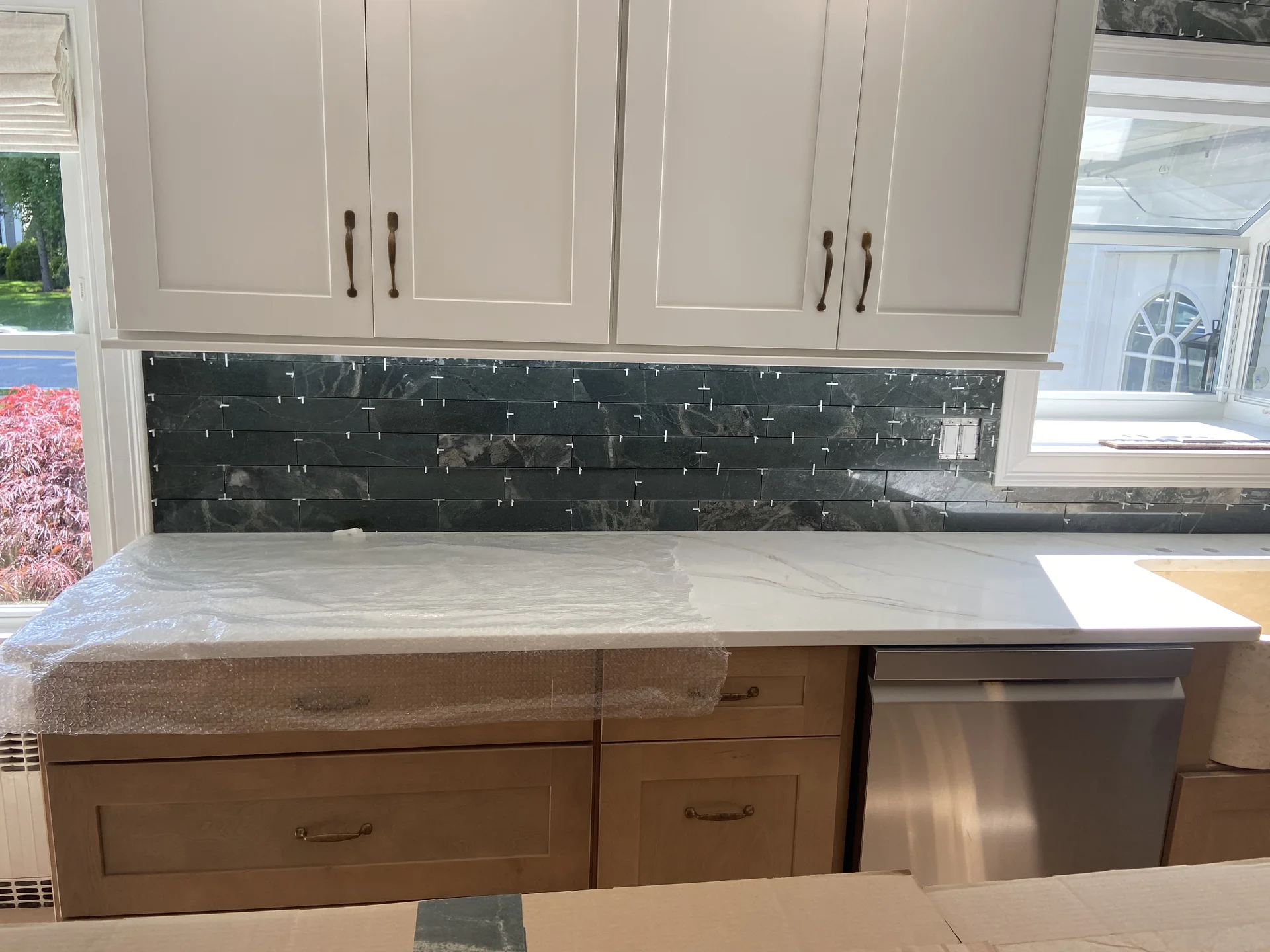 Modern kitchen with white cabinets, black tile backsplash, and light marble countertops by SF Construction in Marlborough, MA
