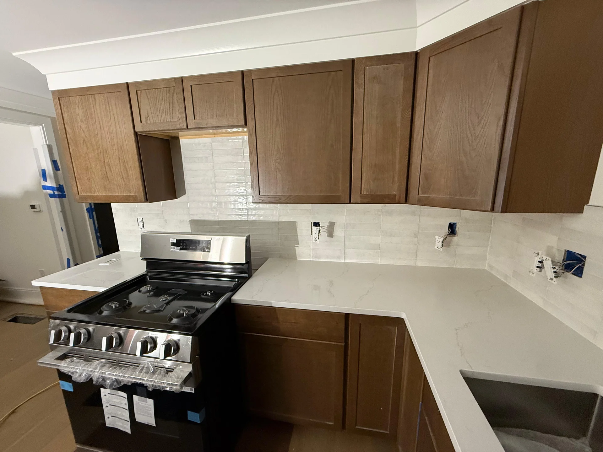 New kitchen with white countertops, brown cabinets, subway tile backsplash, stainless appliances by SF Construction in Marlbo