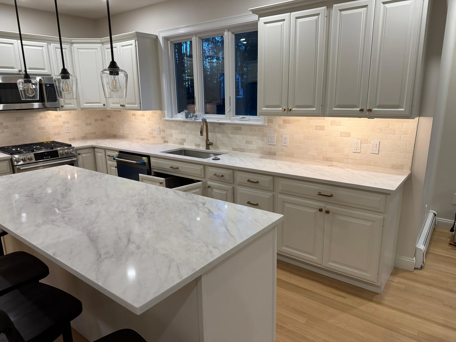 Modern white kitchen with marble countertops, subway tile backsplash, stainless appliances by SF Construction in Northborough