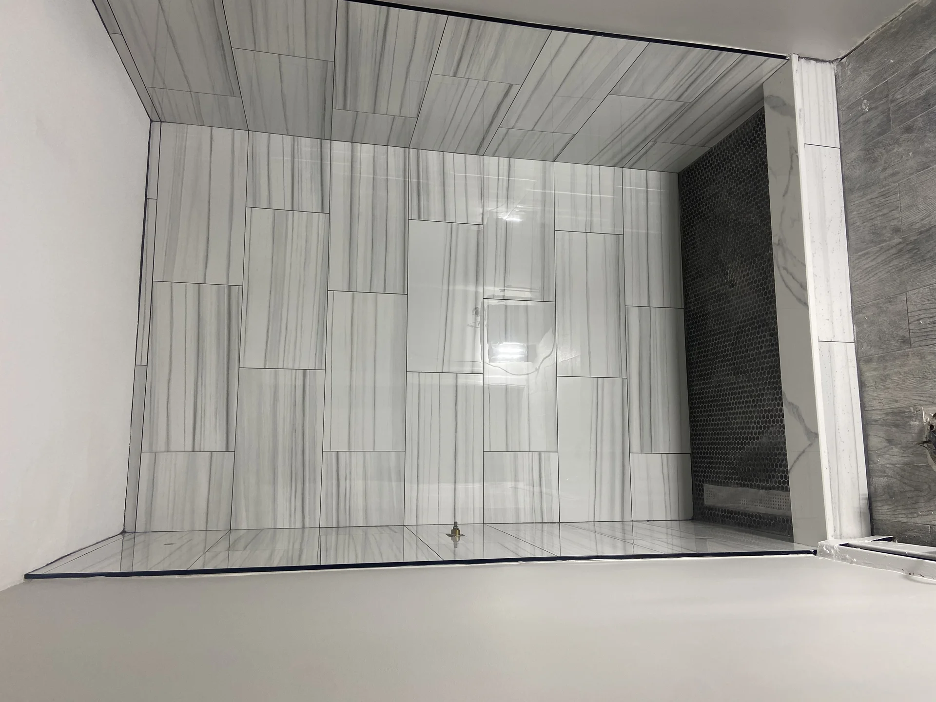 Modern bathroom shower enclosure with gray linear tile walls and glass door by SF Construction in Hudson, MA