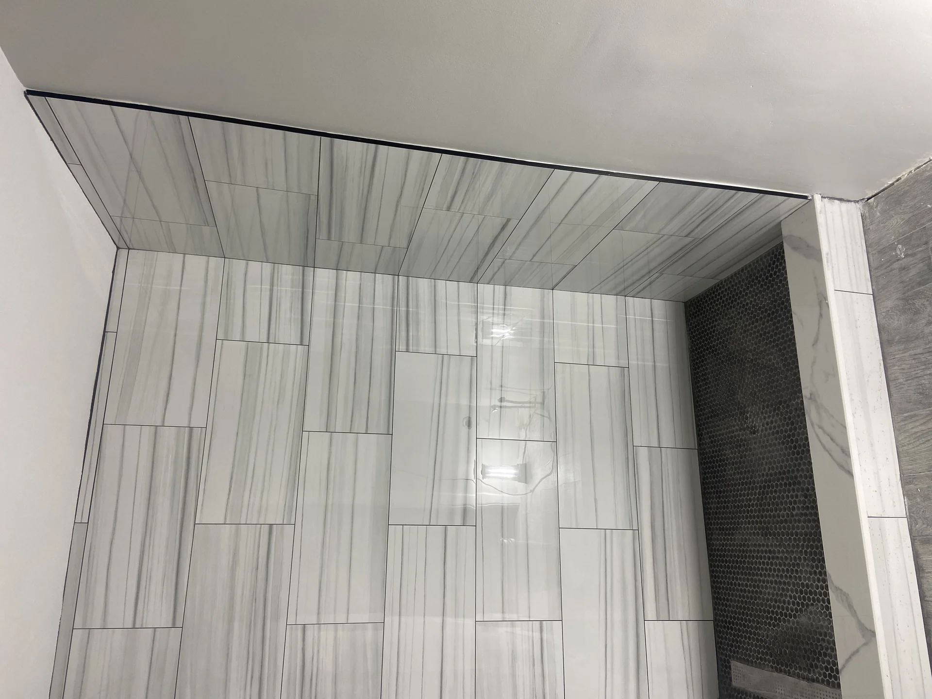 Modern bathroom shower enclosure with gray wood-grain tile walls and dark penny tile accent by SF Construction in Marlborough