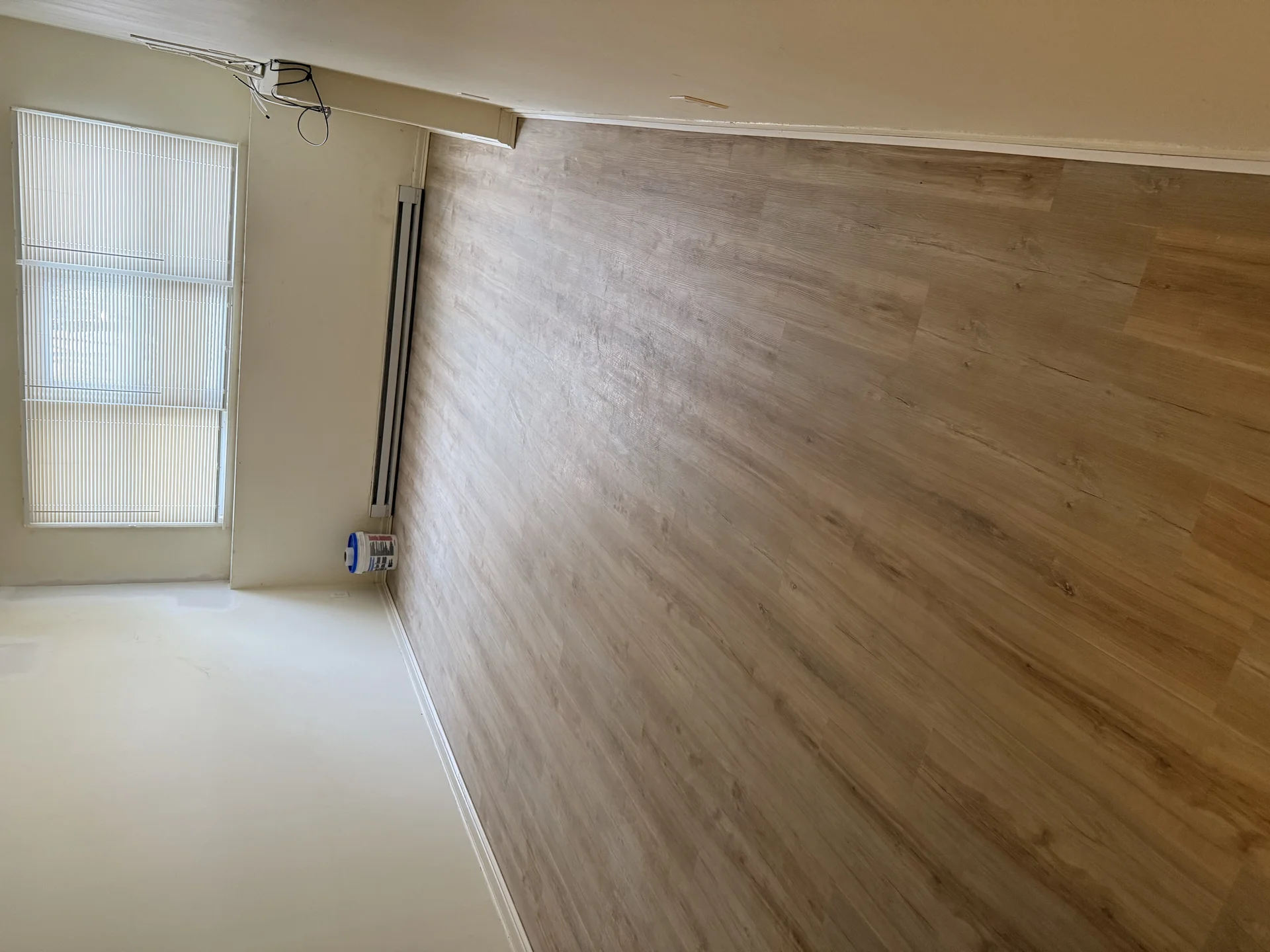Light wood-tone vinyl plank flooring installation in empty room with natural light by SF Construction in Westborough, MA