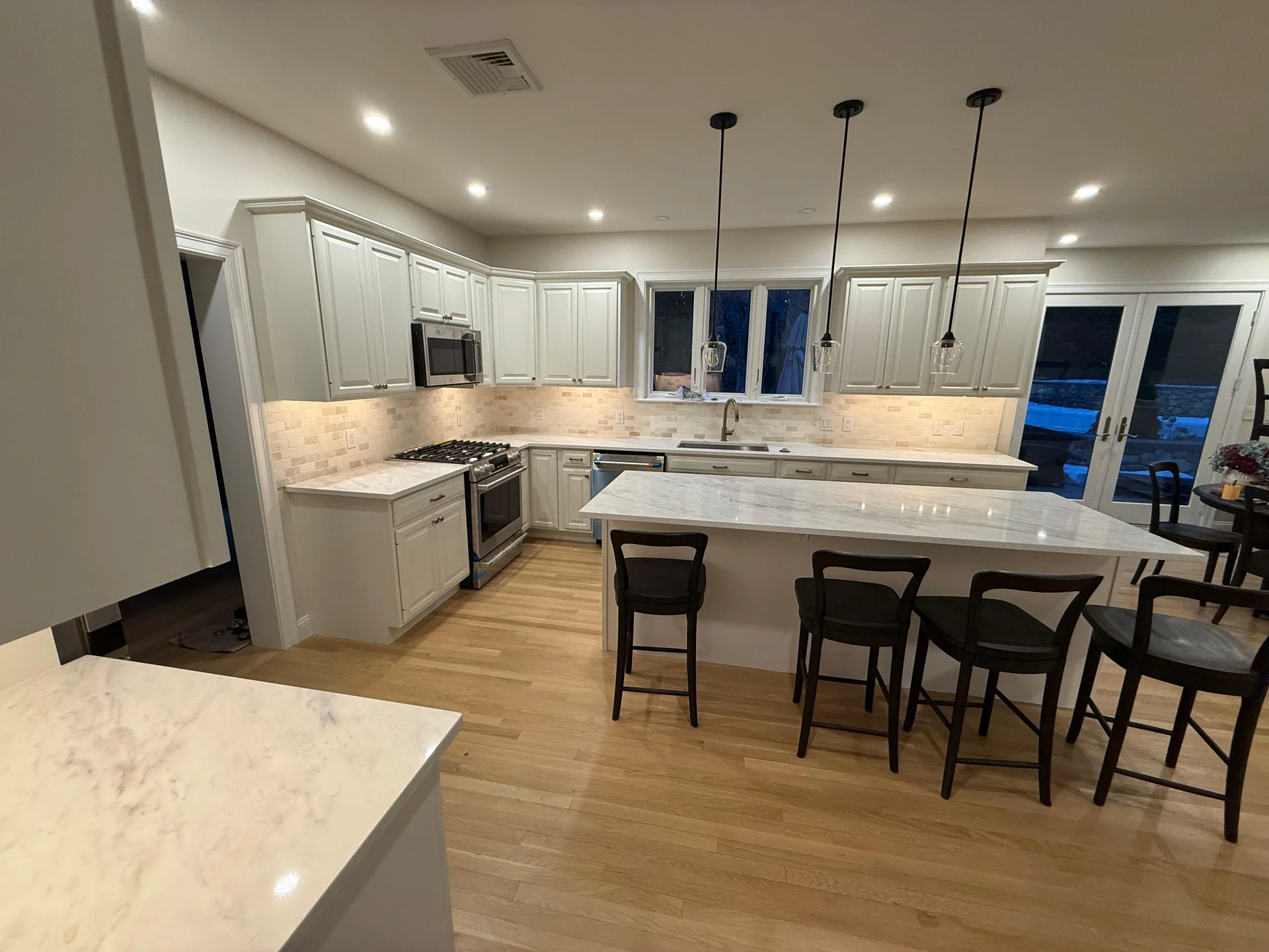 Modern white kitchen with marble countertops, subway tile backsplash, hardwood flooring by SF Construction in Hudson, MA