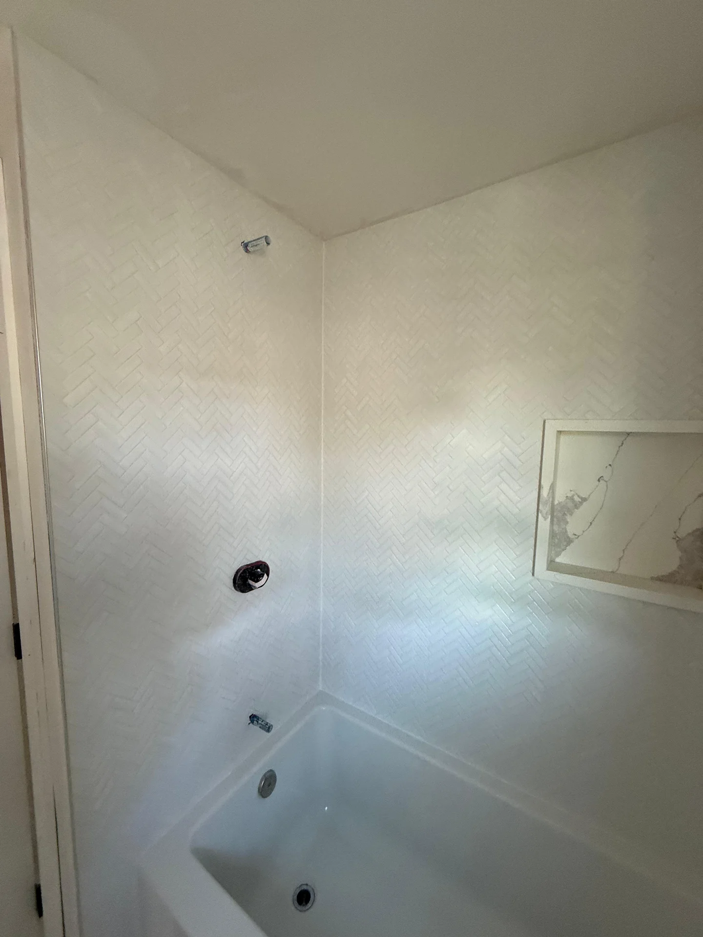 White herringbone tile shower surround with white bathtub and fixtures installed by SF Construction in Sudbury, MA