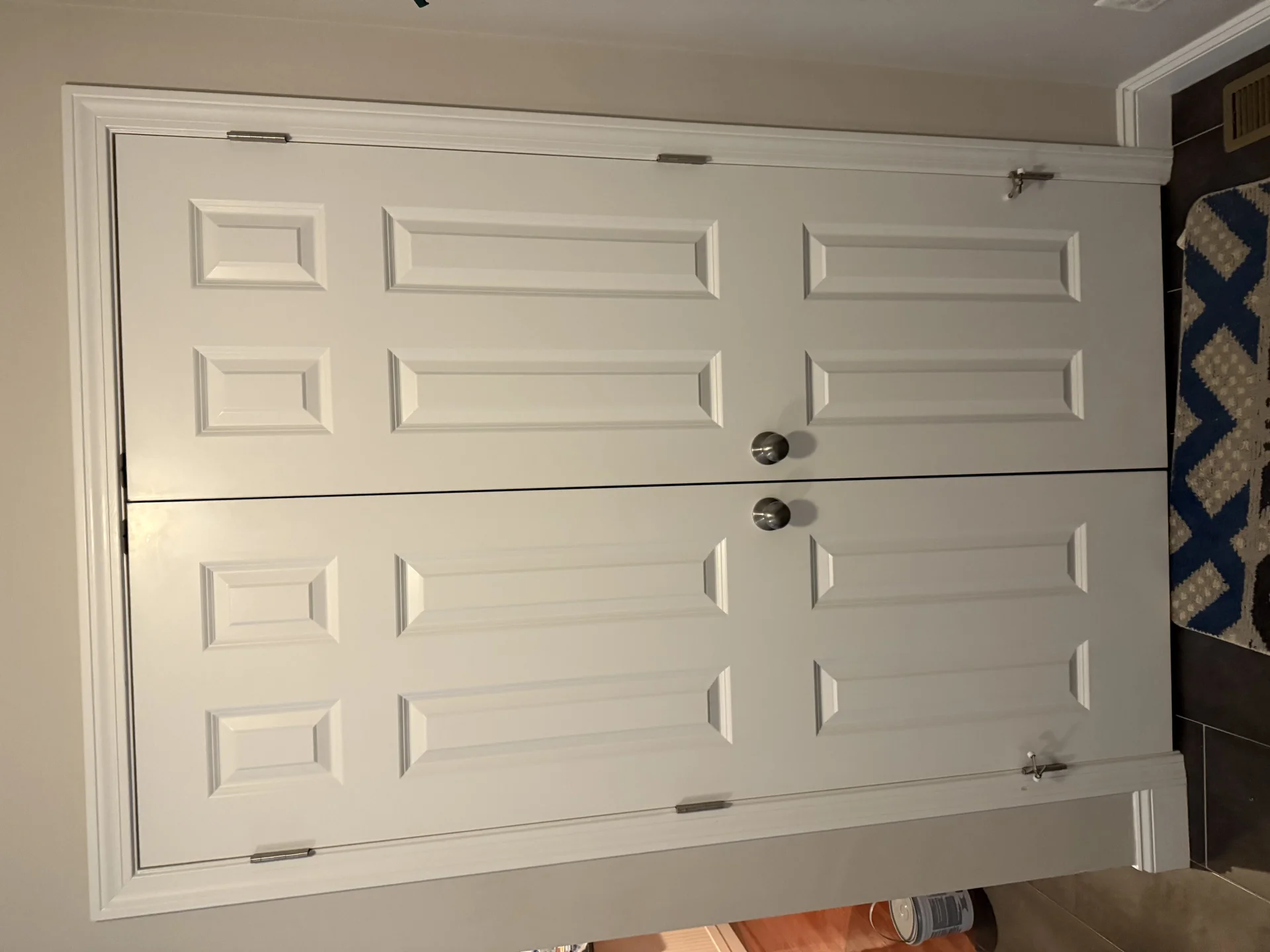 White bi-fold doors with brushed nickel hardware and white trim in a home interior. by SF Construction in Framingham, MA