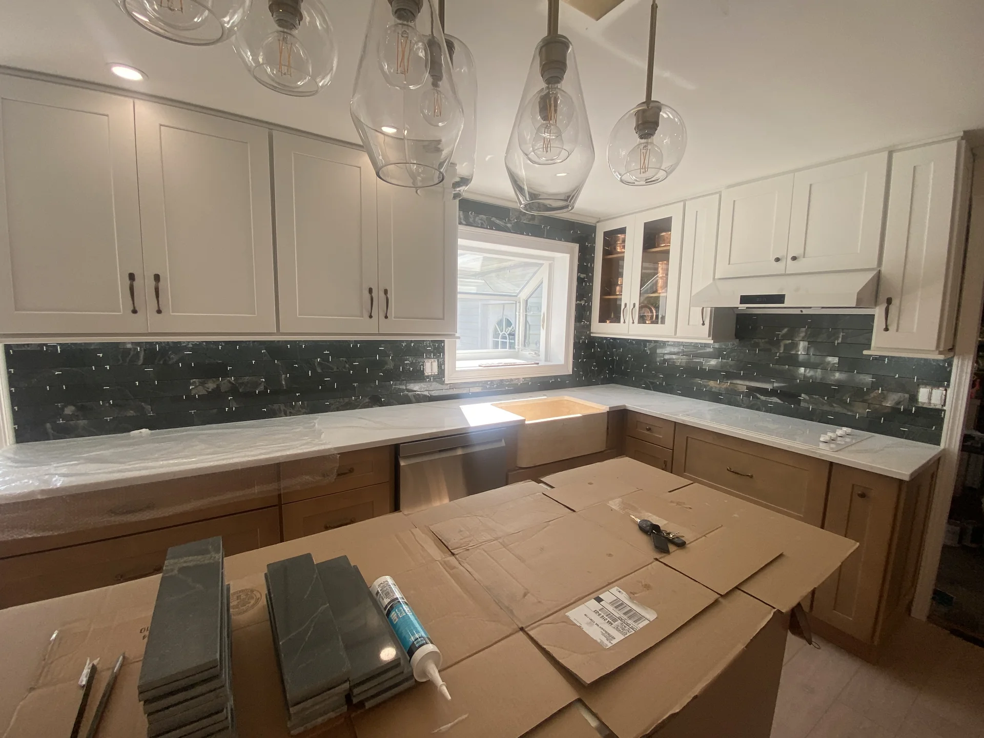 Kitchen renovation with white upper cabinets, wood lower cabinets, dark green backsplash, and white countertops. by SF Constr