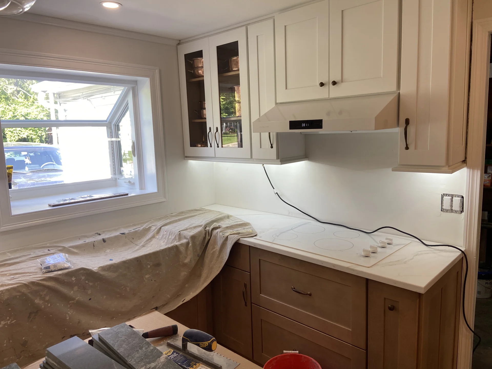 Kitchen under renovation with new white cabinets, light countertops, and a cooktop. by SF Construction in Marlborough, MA