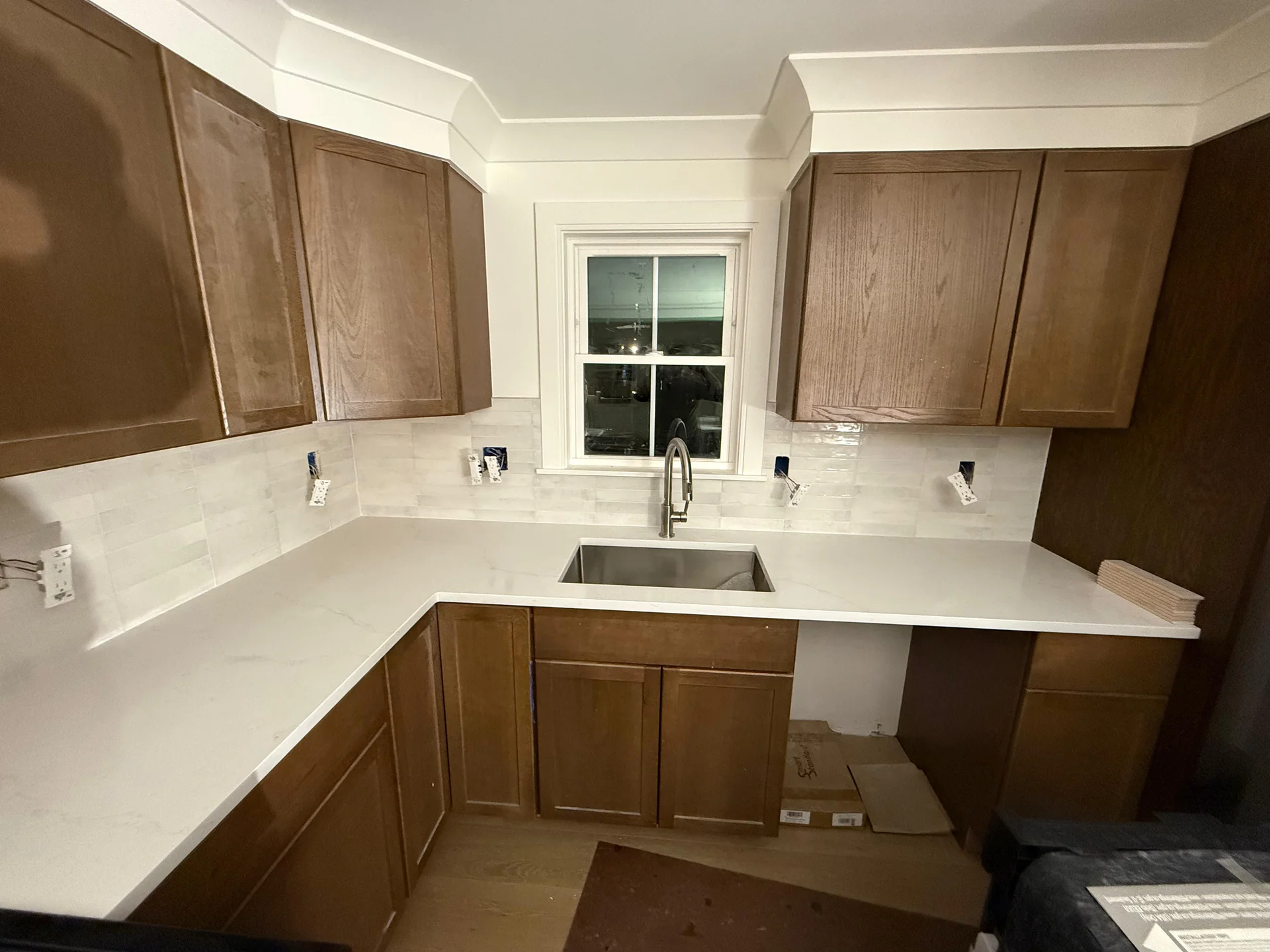 Newly installed brown kitchen cabinets, white quartz countertops, and white subway tile backsplash. by SF Construction in Hud