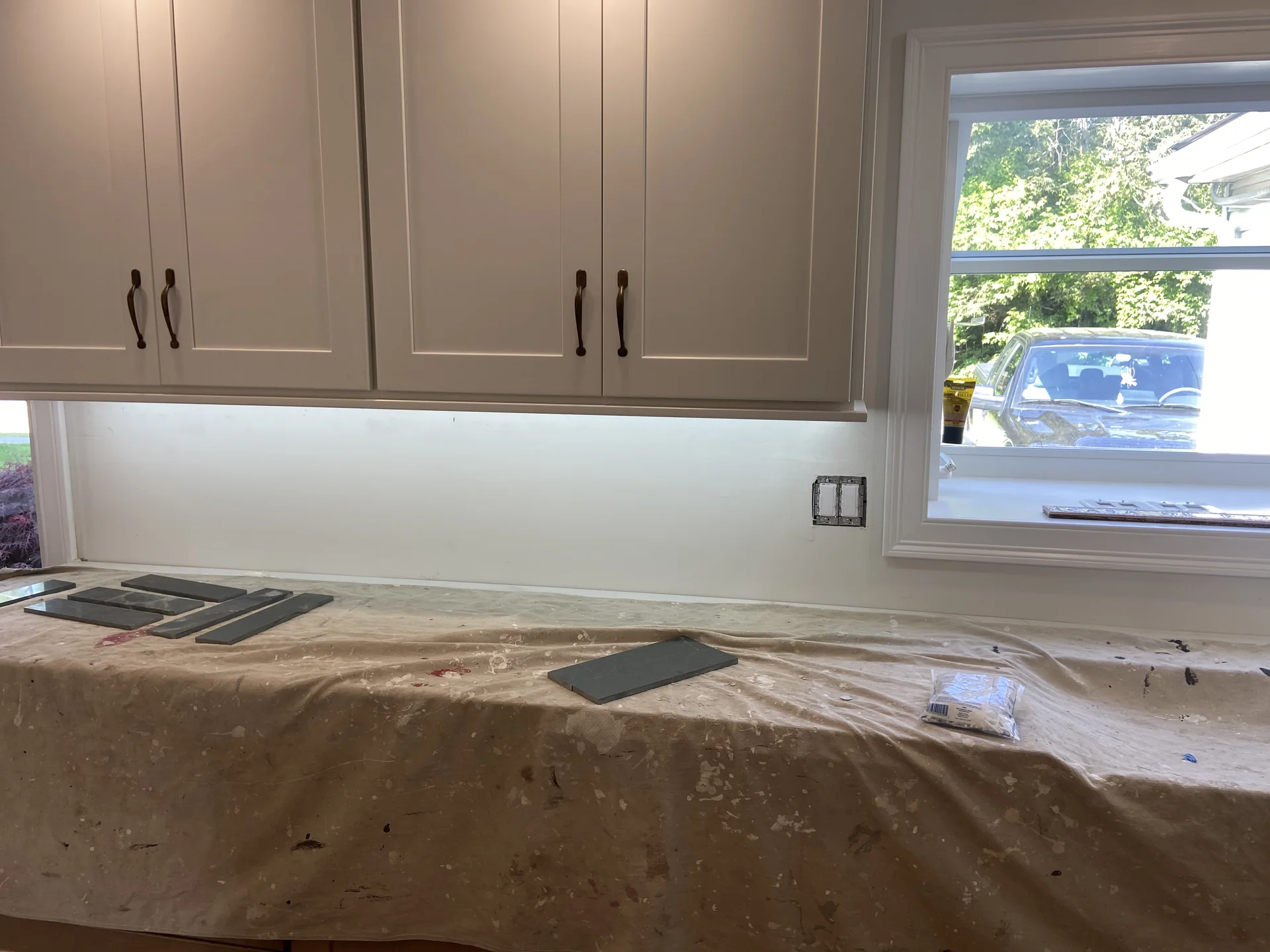 Kitchen renovation in progress with new white cabinets, under-cabinet lighting, and dark gray tiles on a covered countertop.