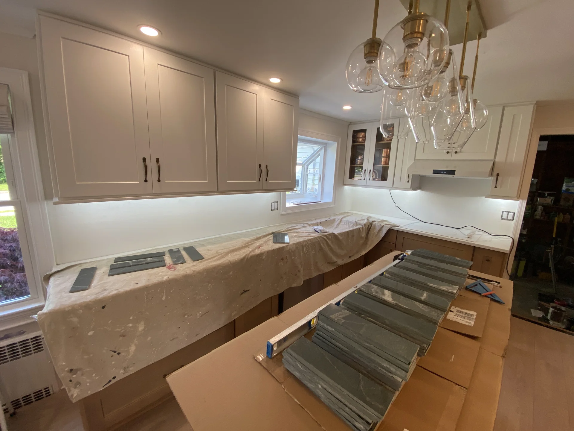 Kitchen renovation in progress with new white cabinets, under-cabinet lighting, and dark gray tiles ready for installation. b