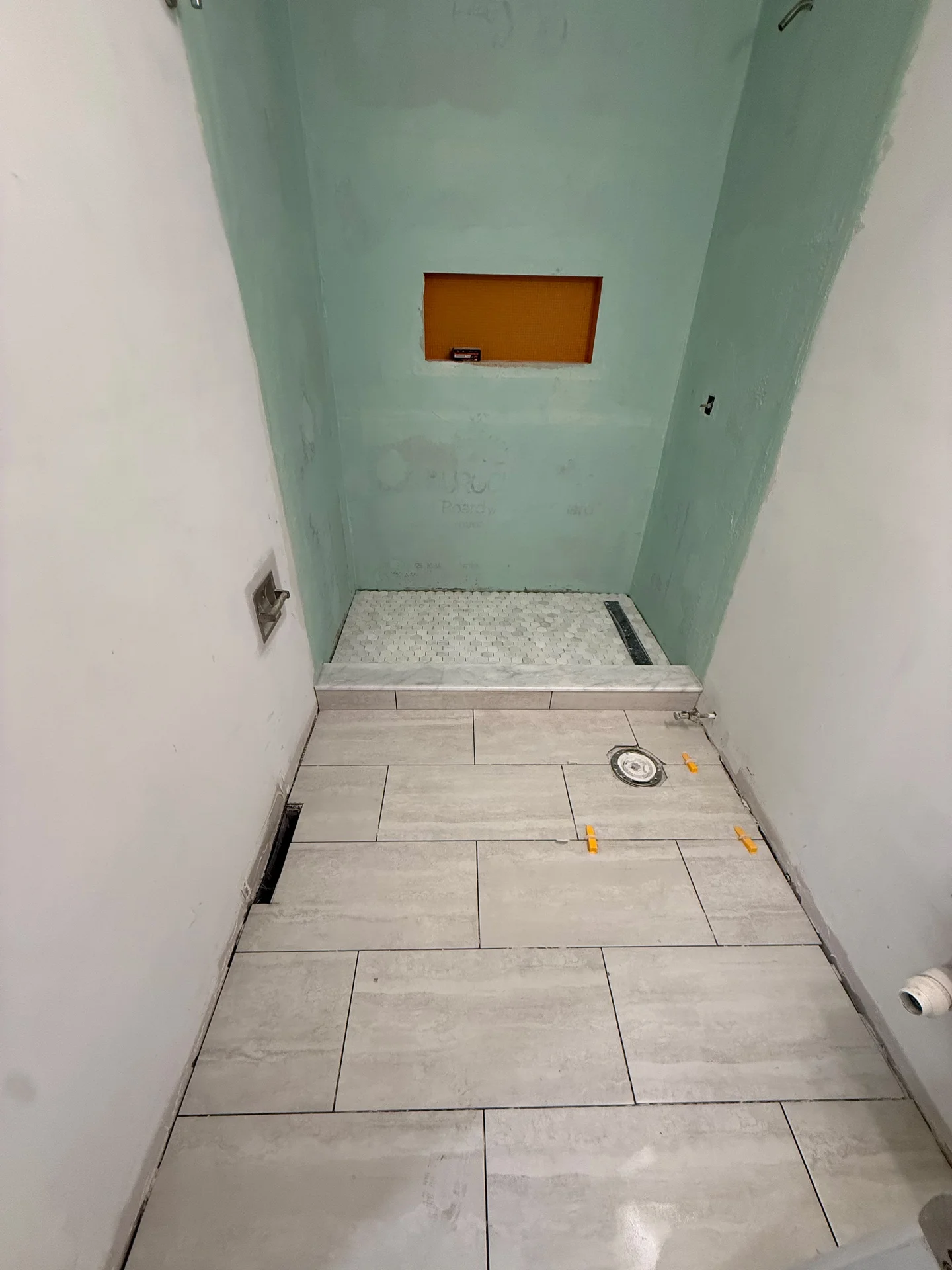 Bathroom under construction with light beige floor tiles, white walls, and green waterproof shower board. by SF Construction