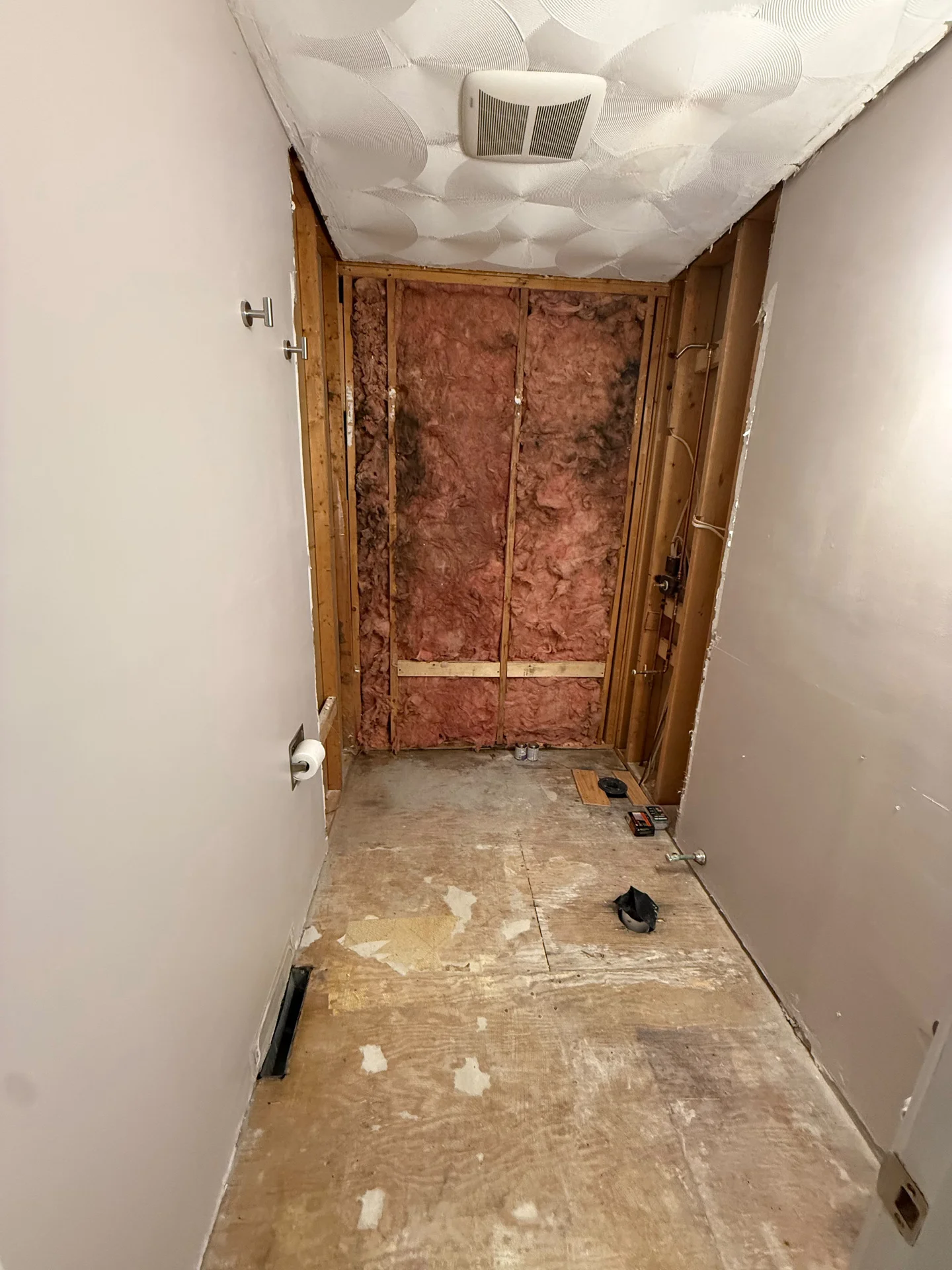 Bathroom under renovation with exposed insulation, wood framing, plywood subfloor, and a textured ceiling. by SF Construction