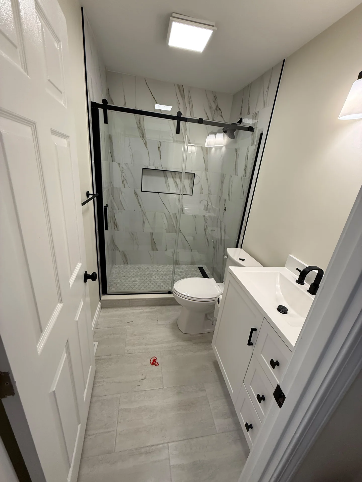 Bright, modern bathroom with white vanity, matte black fixtures, and marble-look shower tiles. by SF Construction in Marlboro