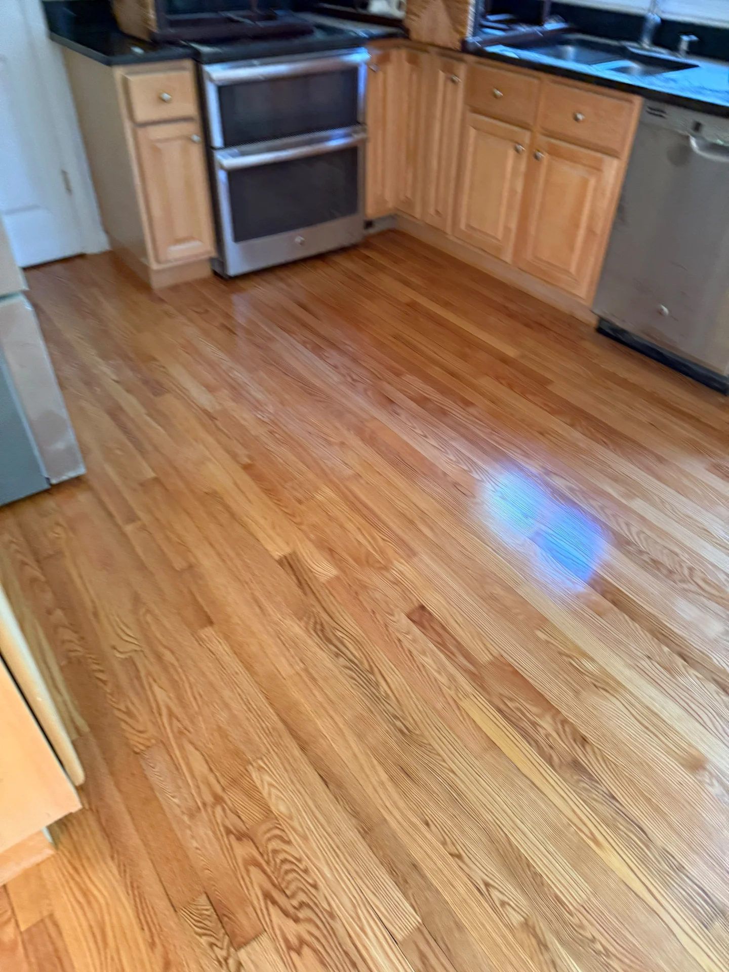 Kitchen with light wood cabinets, black countertops, stainless steel appliances, and wood floors. by SF Construction in Berli
