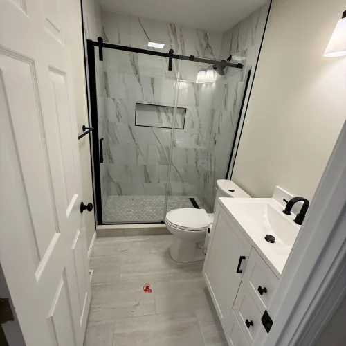 Bright, modern bathroom with white vanity, matte black fixtures, and marble-look shower tiles. by SF Construction in Marlboro