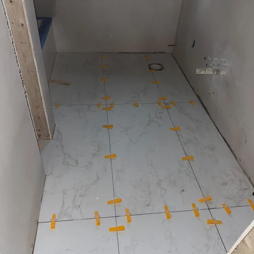 Marble-look ceramic tiles being installed with yellow spacers and grout lines by SF Construction in Marlborough, MA
