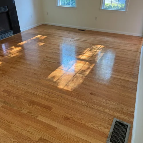Empty room with newly finished hardwood floors, white walls, and a black fireplace. by SF Construction in Hudson, MA