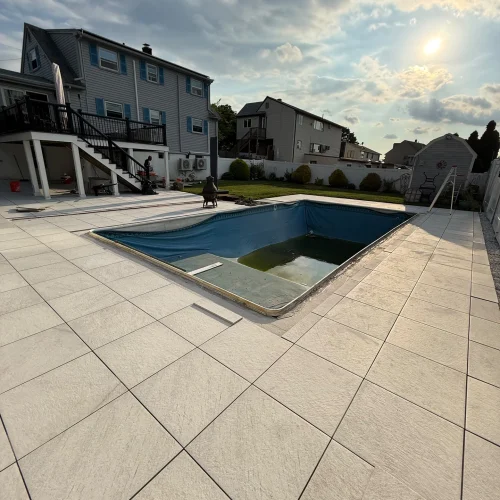 Outdoor patio with large light-colored tiles surrounding a pool under construction. by SF Construction in Westborough, MA