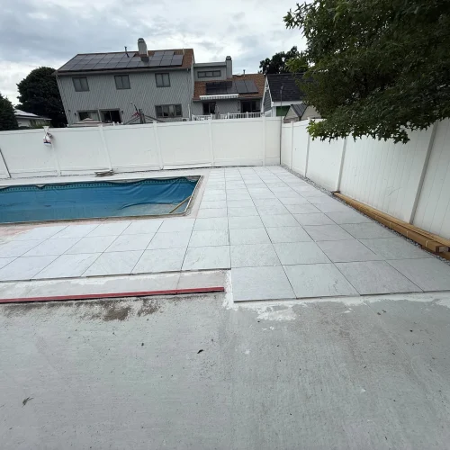 Outdoor scene with a pool and newly laid light grey patio tiles around it. by SF Construction in Berlin, MA
